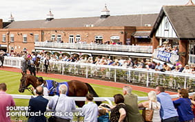 The Grandstand at Pontefract Racecourse with a trainer leading a horse in front of the crowd