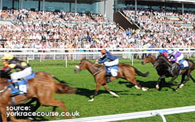 The Grandstand at York Racecourse with a horserace in the foreground