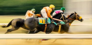 A picture of three horses racing on a sand track.